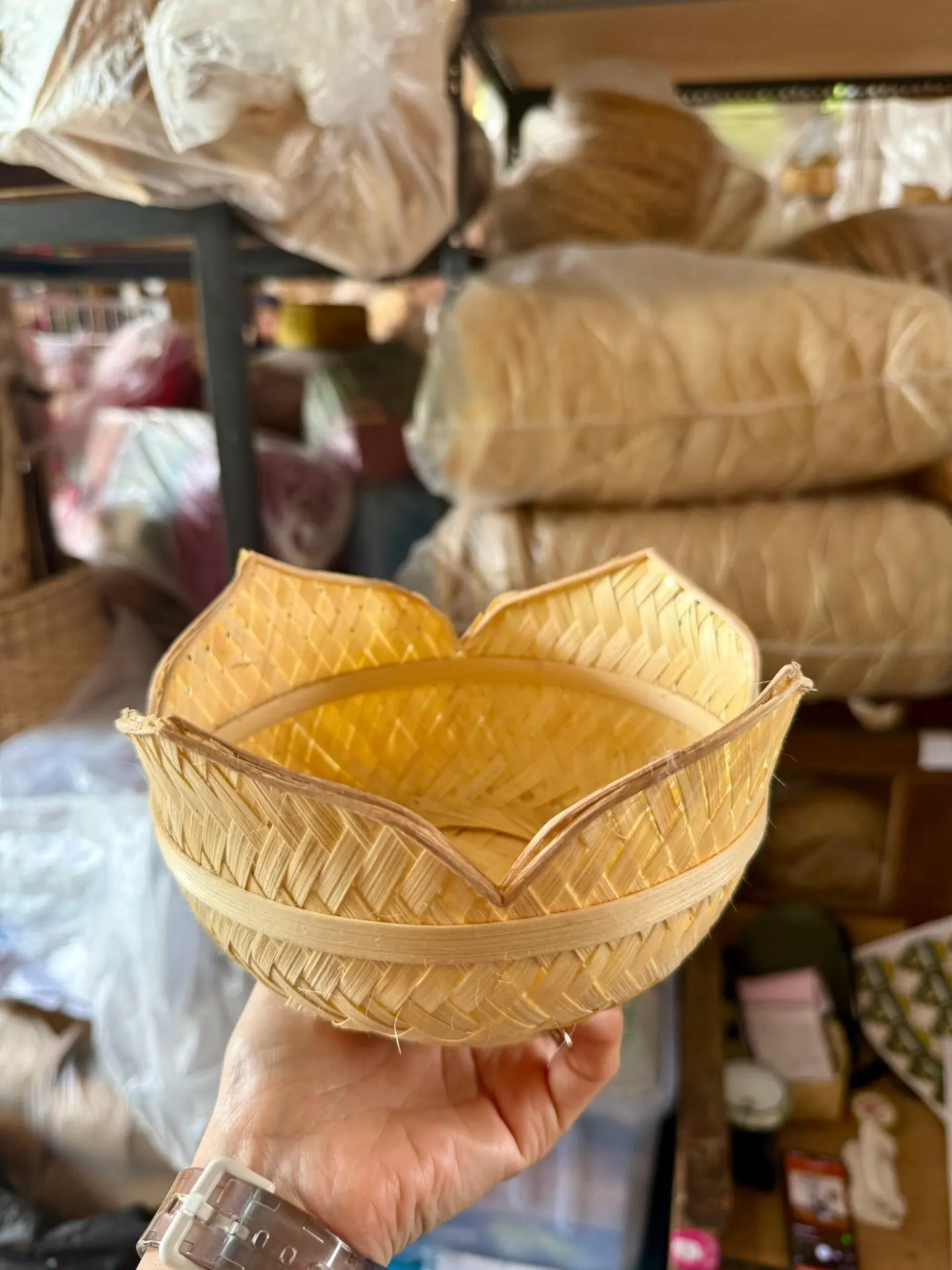 A hand holding a woven bamboo bowl shaped like a lotus