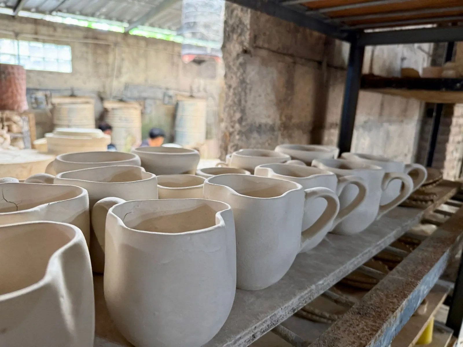 Unfired ceramic mugs drying on shelves